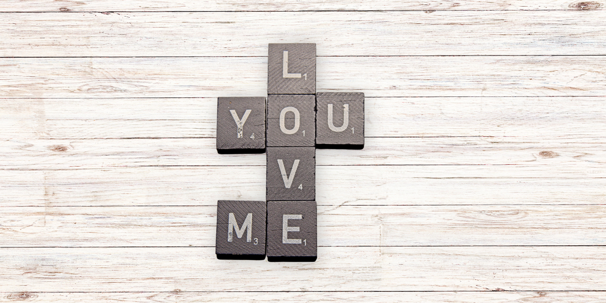 A close-up of a Scrabble game featuring Valentine’s Day words like "LOVE", "ME" and "YOU." The image emphasizes fun literacy activities for families during Valentine's Day.