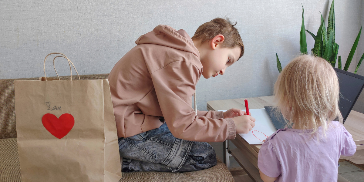 Two children sitting at a desk, using paper, markers, and stickers to create personalized Valentine’s Day cards. The image showcases creative activities that encourage heartfelt expressions.