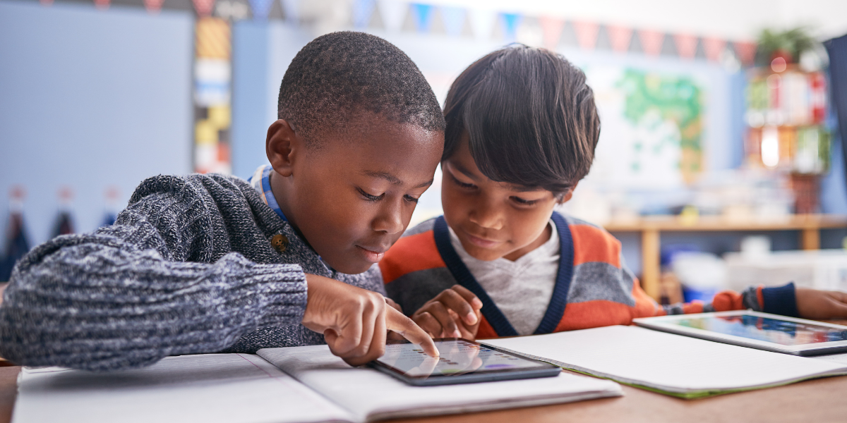 Two young children sitting at their desks in a classroom, focused on completing their homework. The image highlights a structured and collaborative learning environment for young students.