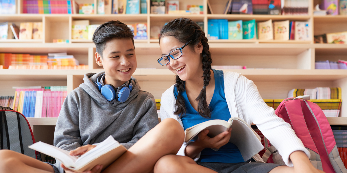 Two teenagers sitting together in a library, deeply engrossed in books. The image highlights the importance of library visits to foster literacy and encourage independent reading skills in teens.