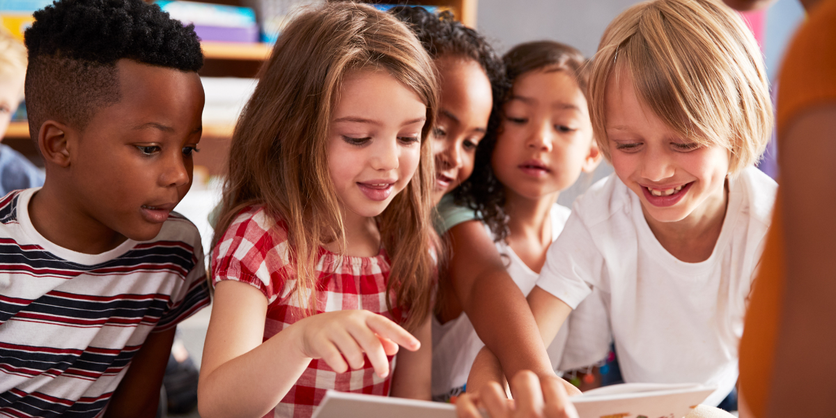 A group of young children sitting in a classroom, enthusiastically participating in a reading lesson with their teacher. The scene emphasizes the value of early literacy education and group learning.