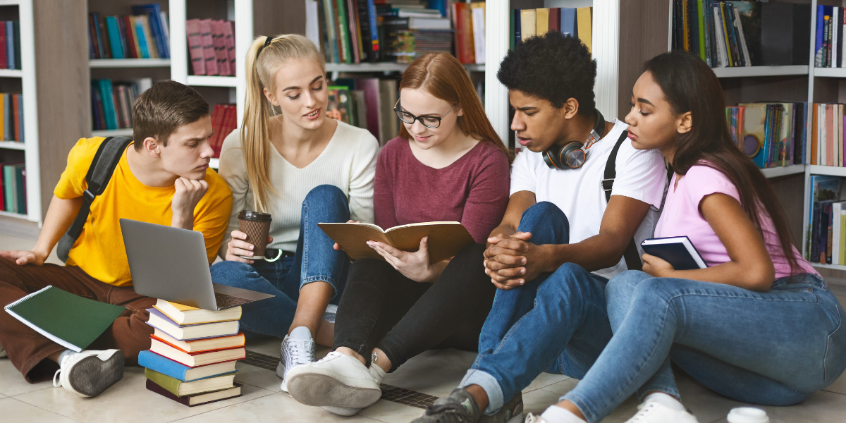 A group of teenagers seated in a library, reading books individually. This image reflects the role of libraries in promoting a love for reading and improving literacy skills among teens.