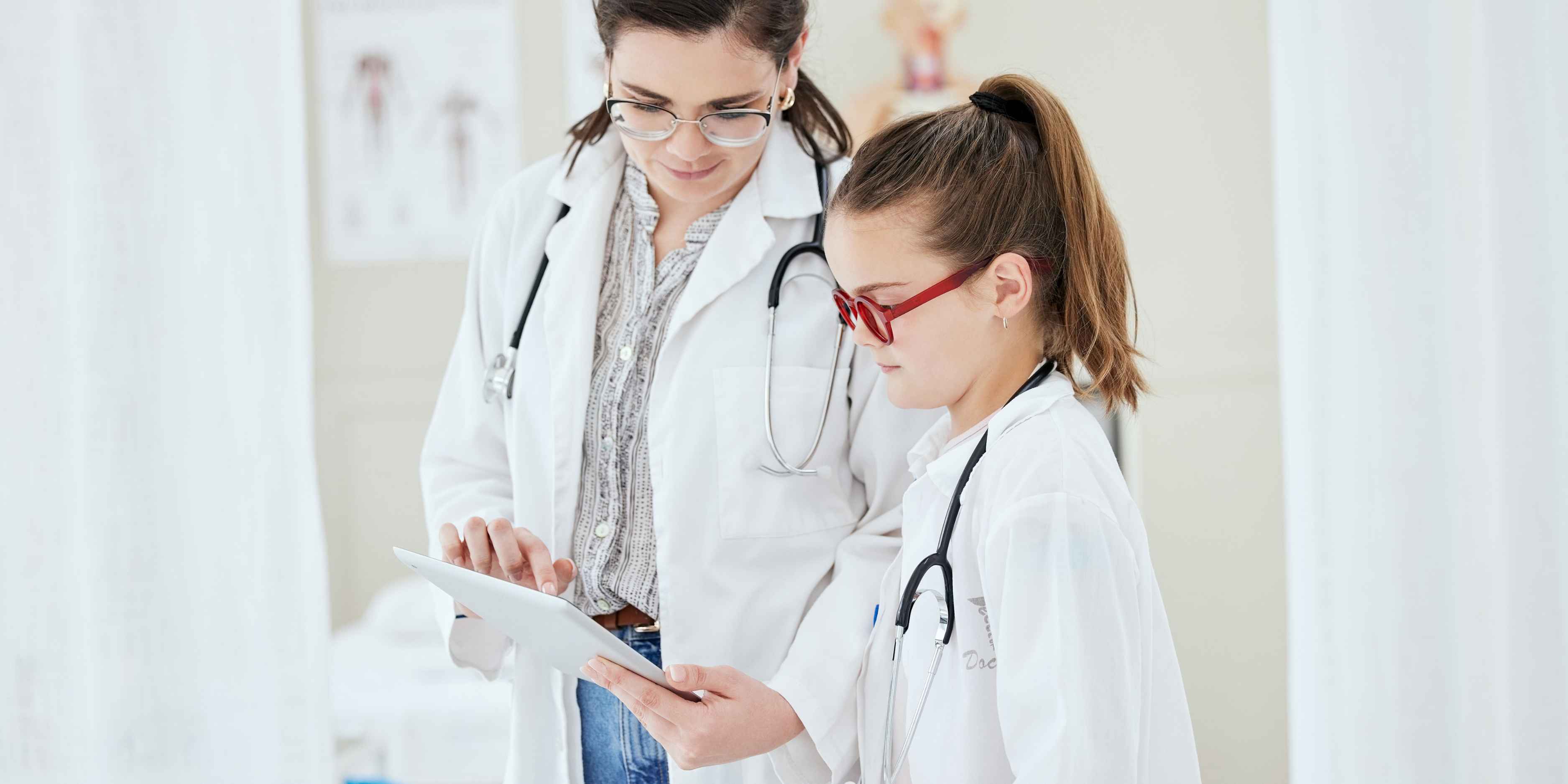 A parent and child dressed as doctors, using a toy stethoscope to role-play a medical exam, highlighting career exploration through pretend play.