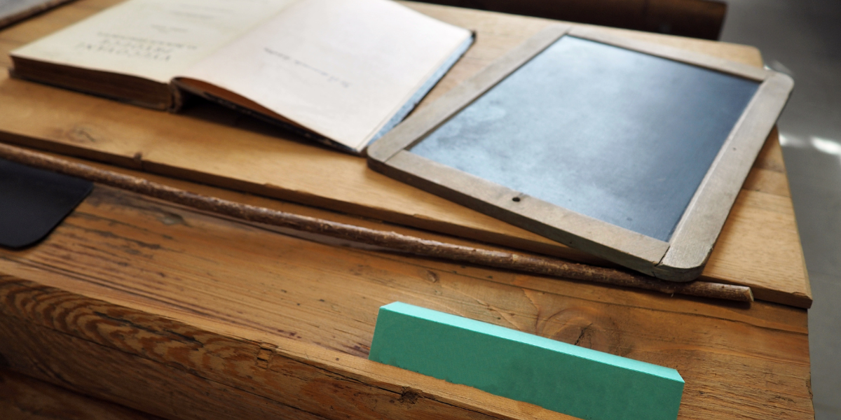 A desk in the 1700s with historical school supplies on top, including hornbooks and quill pens, as they practice reading and writing.